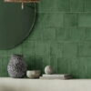 A green tile wall featuring Solar Forest Matt tiles, a round mirror, and a stylish vase adds a fresh touch to the space.